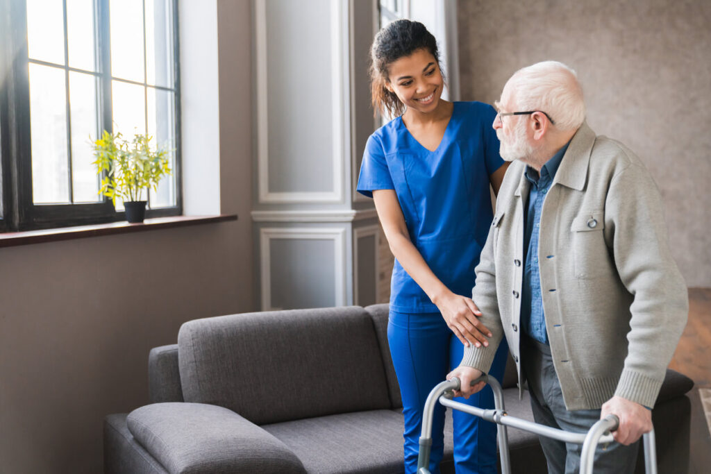 Young nurse helping old elderly disable man grandfather to walk using walker equipment