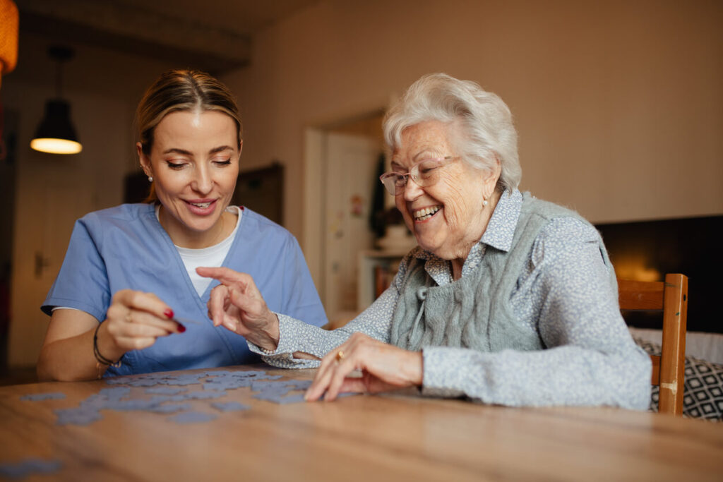 Friendly caregiver and elderly patient working on puzzle together